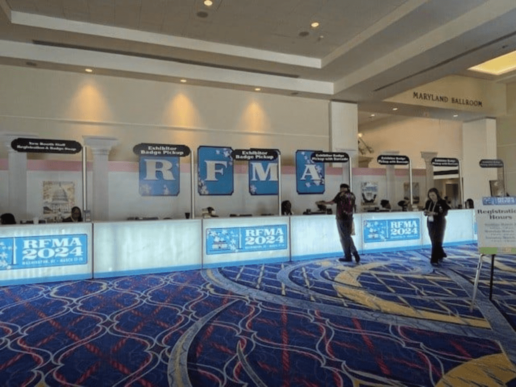Conference registration counters with illuminated panels and staff.
